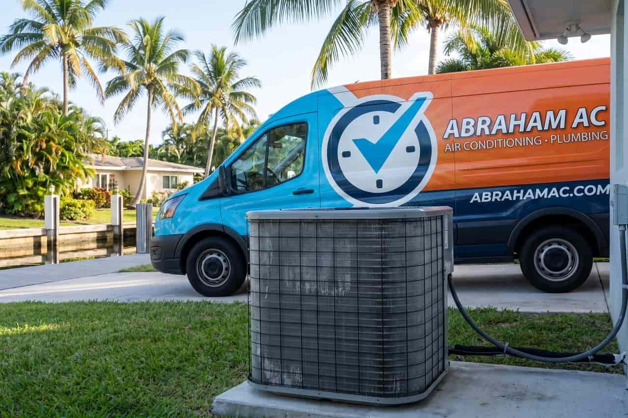 Outdoor heat pump on a lawn with a service van parked in the driveway